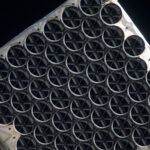 : NICER’s X-ray concentrators are dark circles in eight staggered rows covering this image. Each one is divided into six segments, like a sliced pie, by its sunshade. The concentrators rest in a white frame of the telescope.