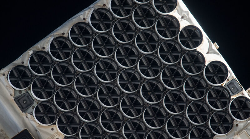 : NICER’s X-ray concentrators are dark circles in eight staggered rows covering this image. Each one is divided into six segments, like a sliced pie, by its sunshade. The concentrators rest in a white frame of the telescope.